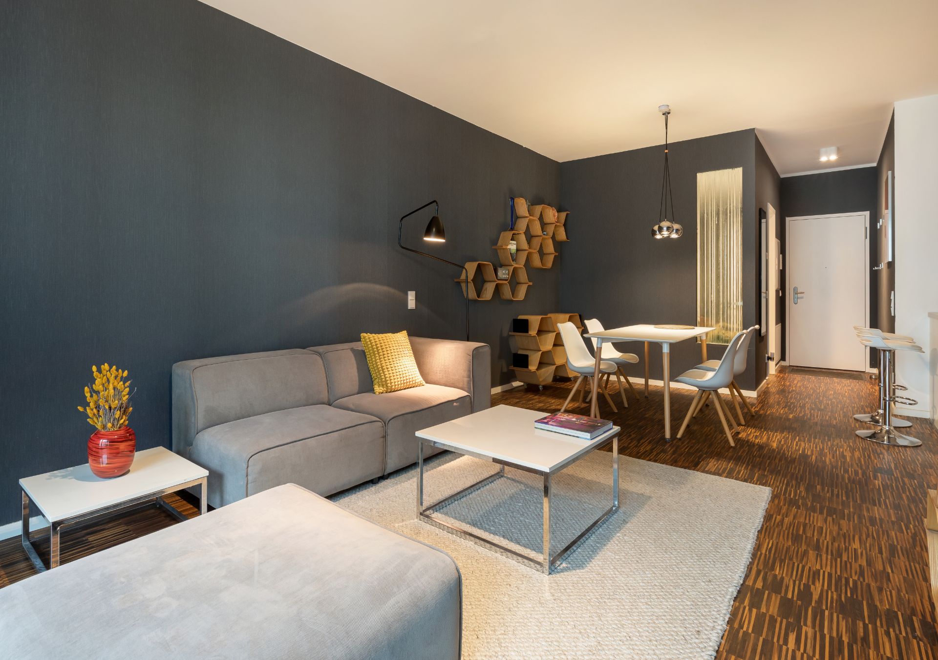 Modernes Wohnzimmer mit grauem Sofa, Teppich, Couchtisch und Essbereich mit vier Stühlen.