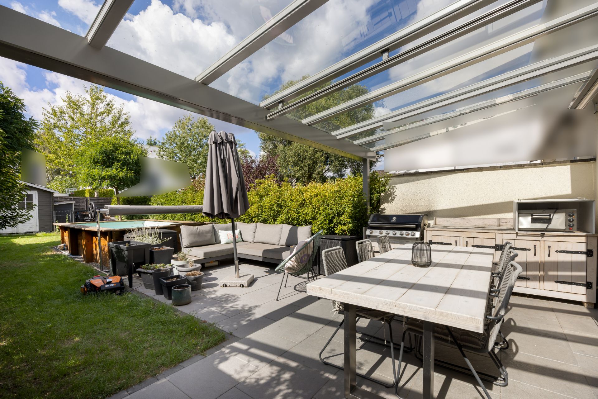 Überdachte Terrasse mit Esstisch, Stühlen, Grillecke und Lounge-Sofa im Garten.