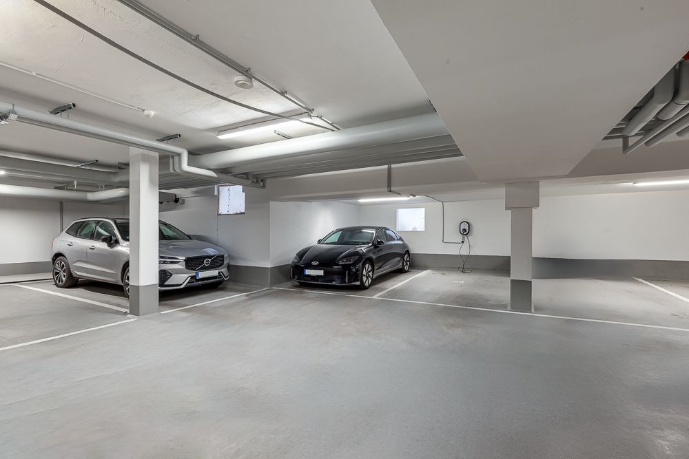 Helle Tiefgarage mit zwei geparkten Autos und Ladestation an der Wand.