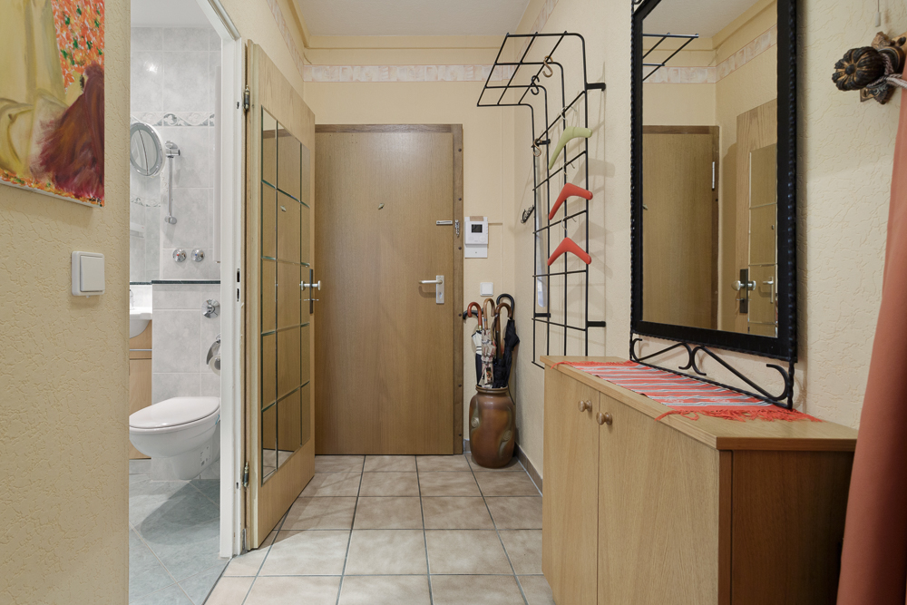Flur mit Holzschrank, großem Spiegel, Garderobe und offenem Blick ins Badezimmer.