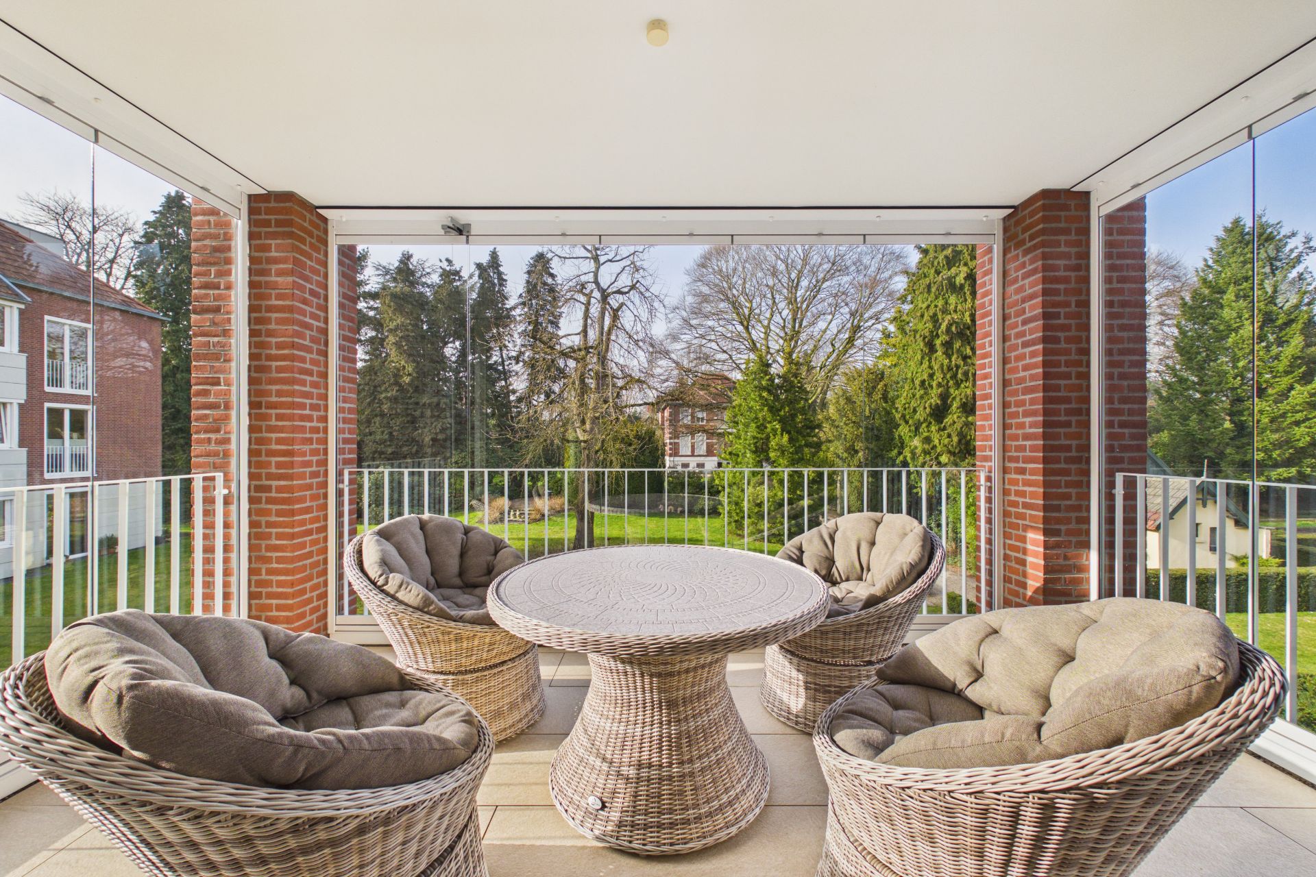 Überdachter Balkon mit vier runden Korbsesseln und einem runden Tisch, Blick auf grünen Garten.