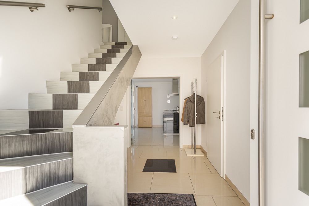 Heller Flur mit Treppe, Kleiderständer, Fliesenboden und Blick in die Küche.