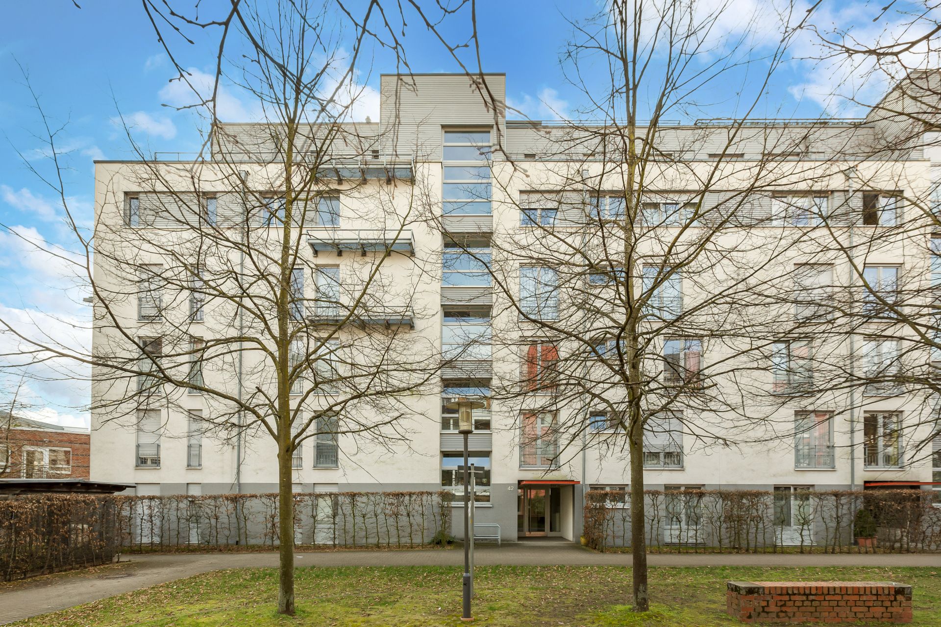 Mehrstöckiges Wohngebäude mit kahlen Bäumen davor und Eingangsbereich in der Mitte.