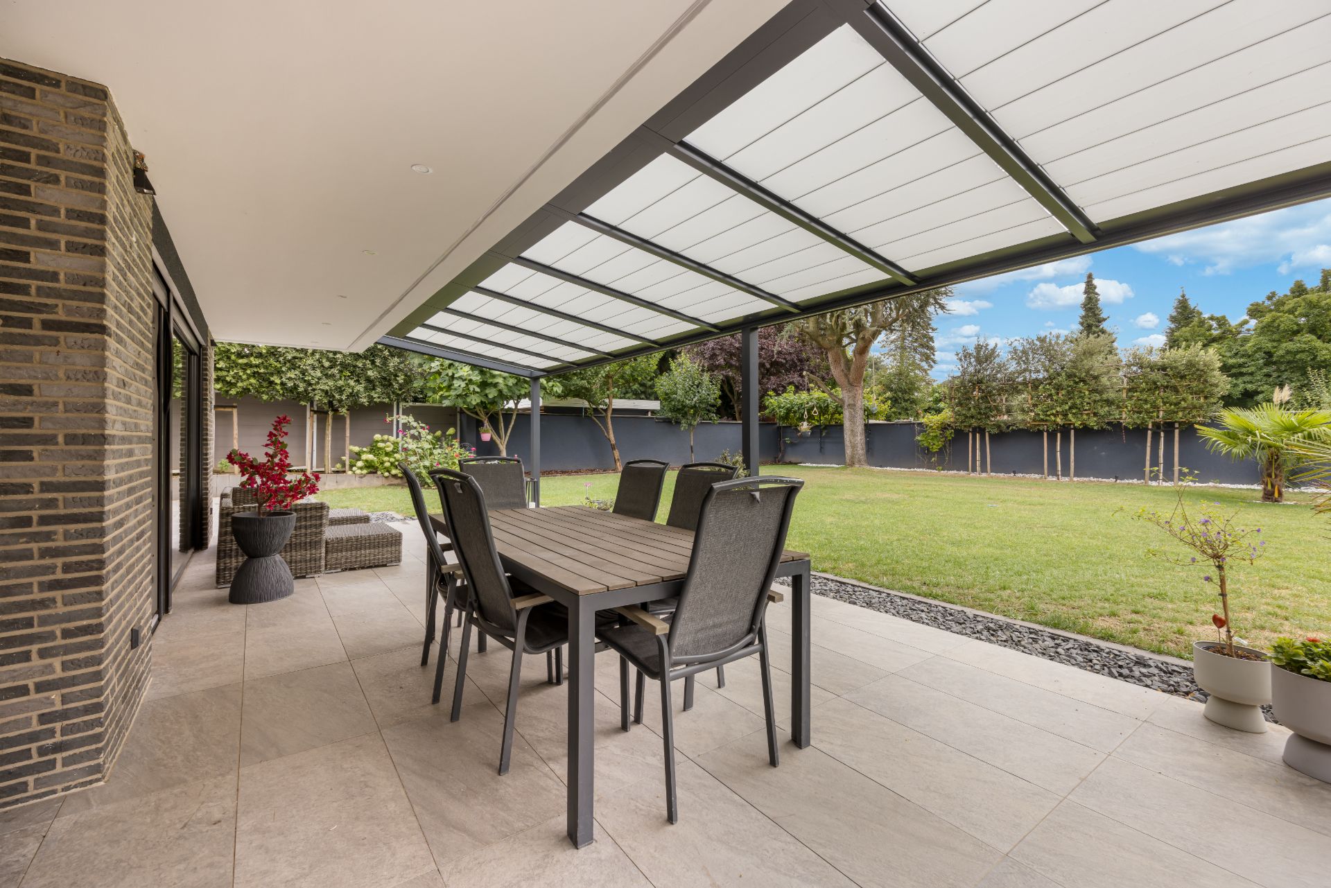 Überdachte Terrasse mit Esstisch, Stühlen und Blick auf gepflegten Garten.