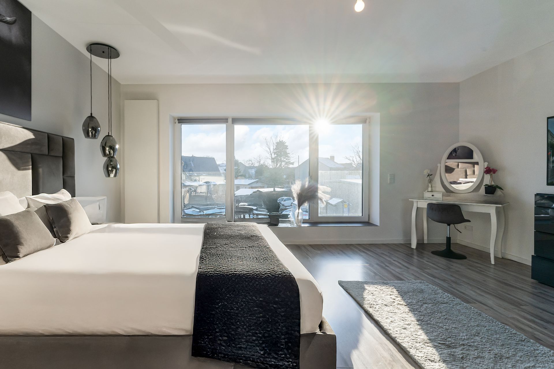 Modernes Schlafzimmer mit großem Bett, Schreibtisch, Teppich und bodentiefen Fenstern mit Blick nach draußen.
