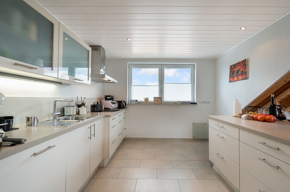 Helle, moderne Küche mit weißen Schränken, Geräten und großem Fenster.