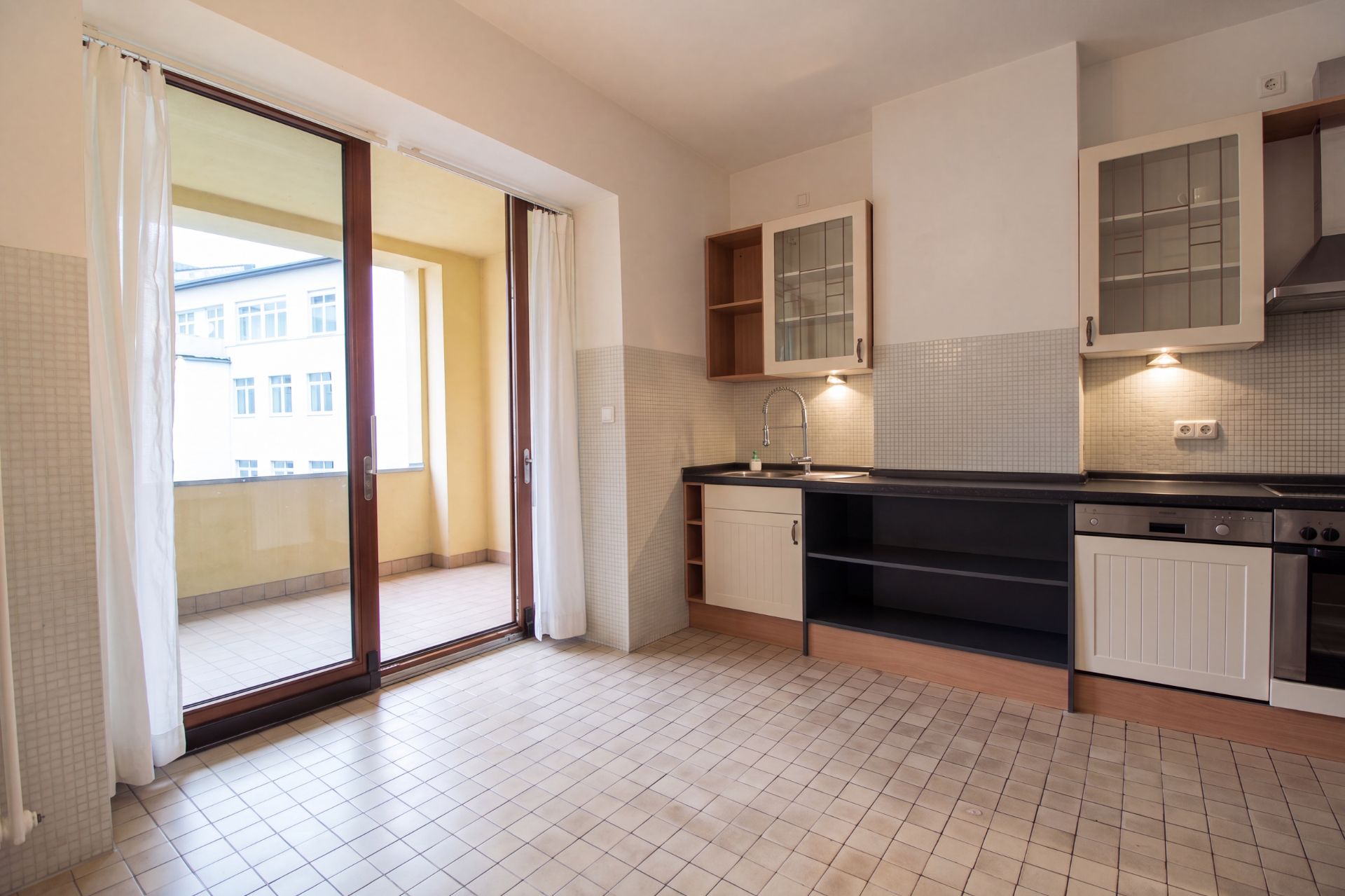 Helle Küche mit Fliesenboden, Einbauküche und Zugang zu einem überdachten Balkon.