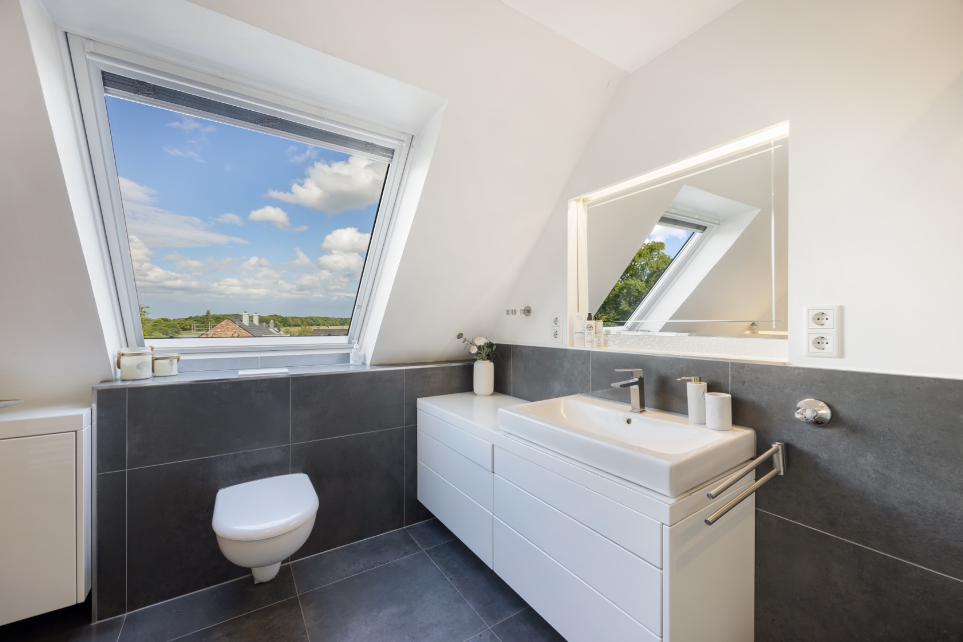 Modernes Badezimmer mit großem Fenster, Waschtisch, Spiegel und Wandtoilette.