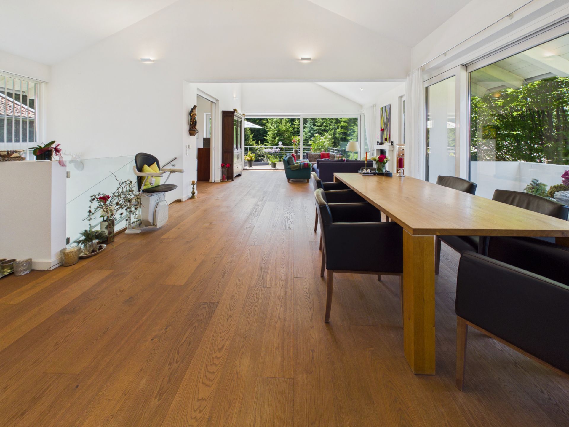 Großes, helles Wohnzimmer mit Holzboden, Esstisch, Stühlen und großen Fenstern zur Terrasse.