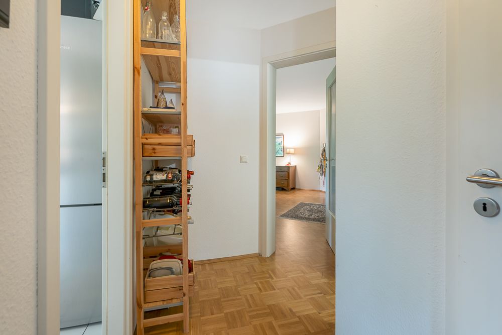Flur mit Holzregal, Blick in helles Wohnzimmer mit Teppich und Möbeln.