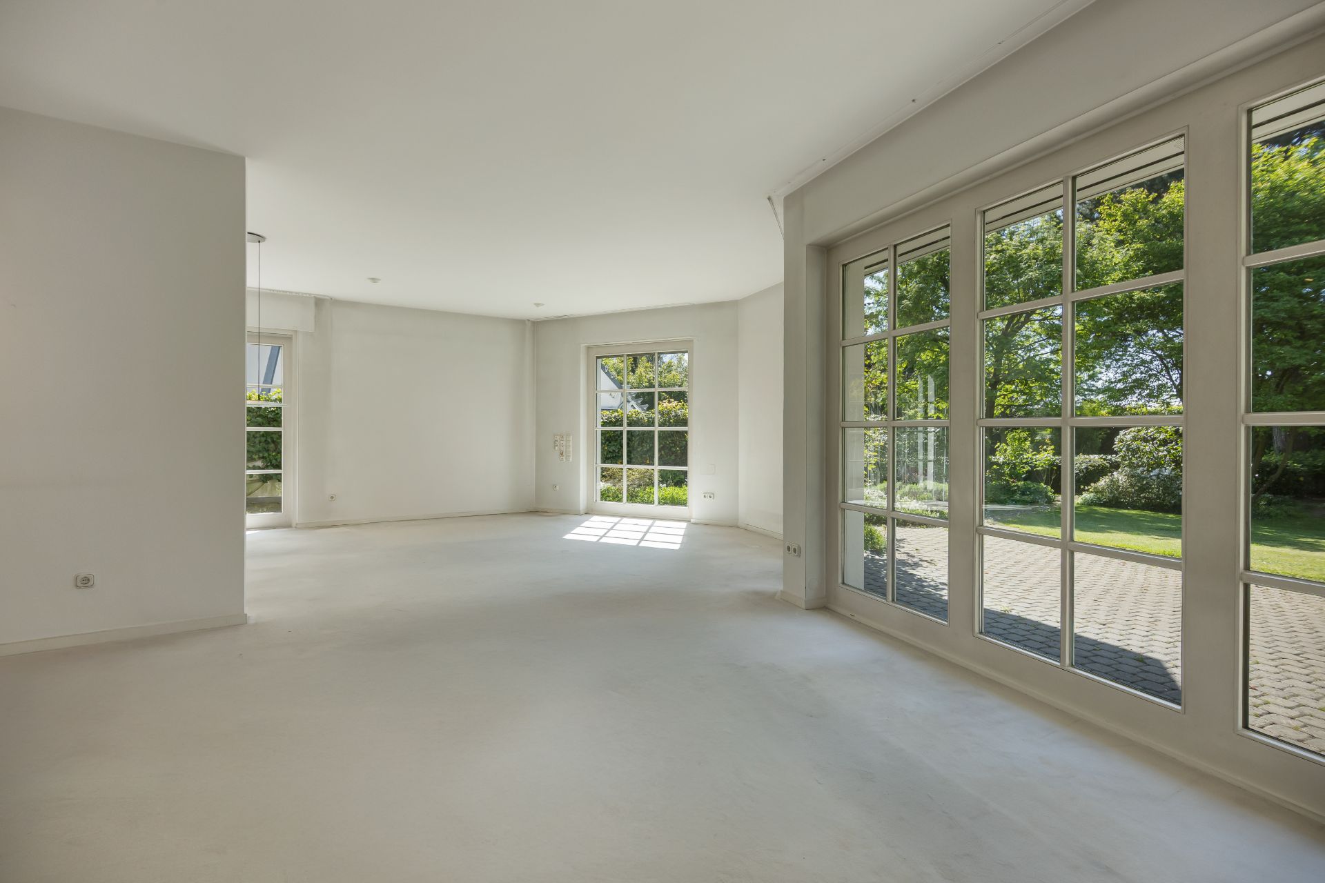 Heller, leerer Raum mit großen Fenstern und Blick in einen grünen Garten.