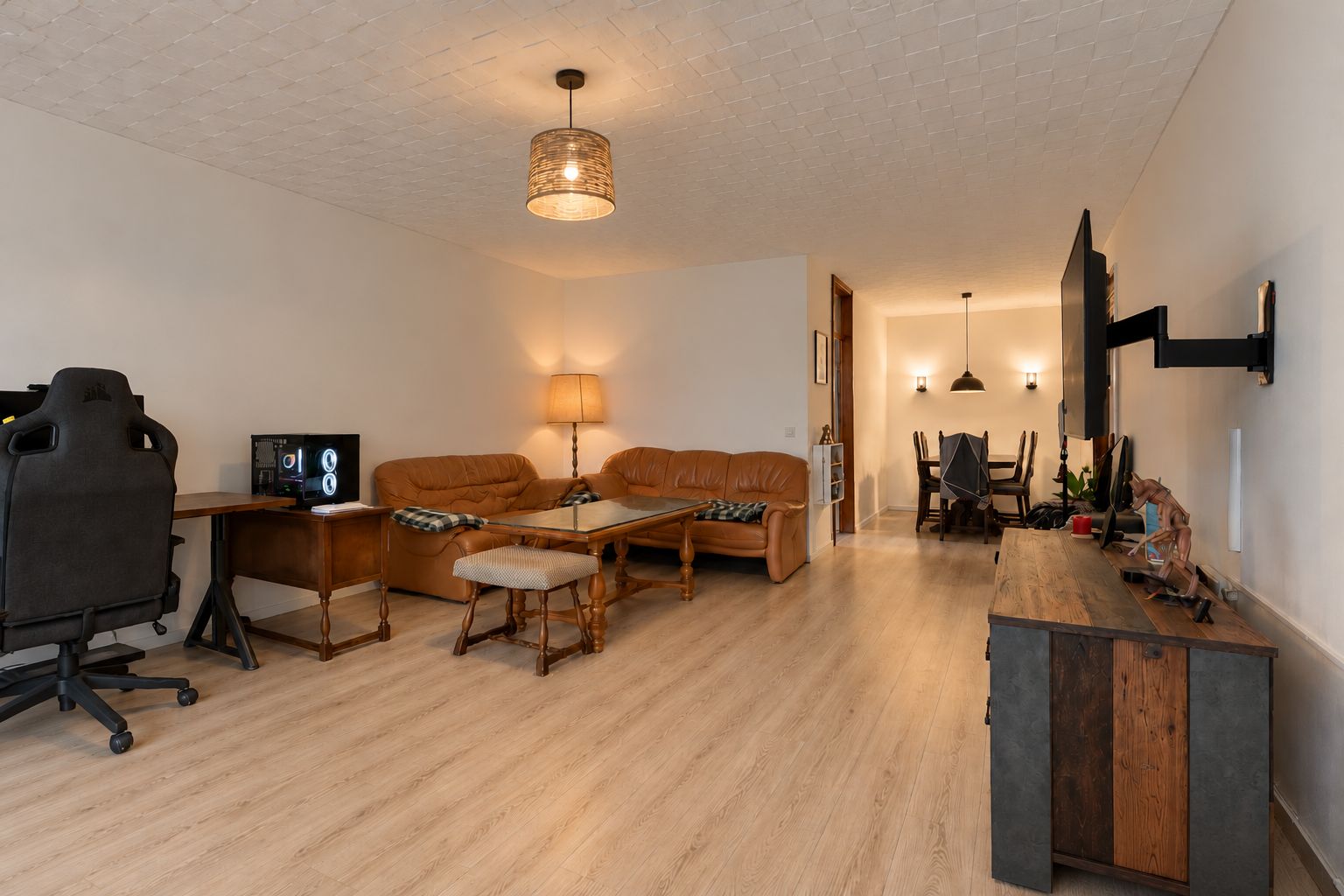Wohnzimmer mit Holzfußboden, Sofa, Schreibtisch mit Stuhl und Fernseher an der Wand.