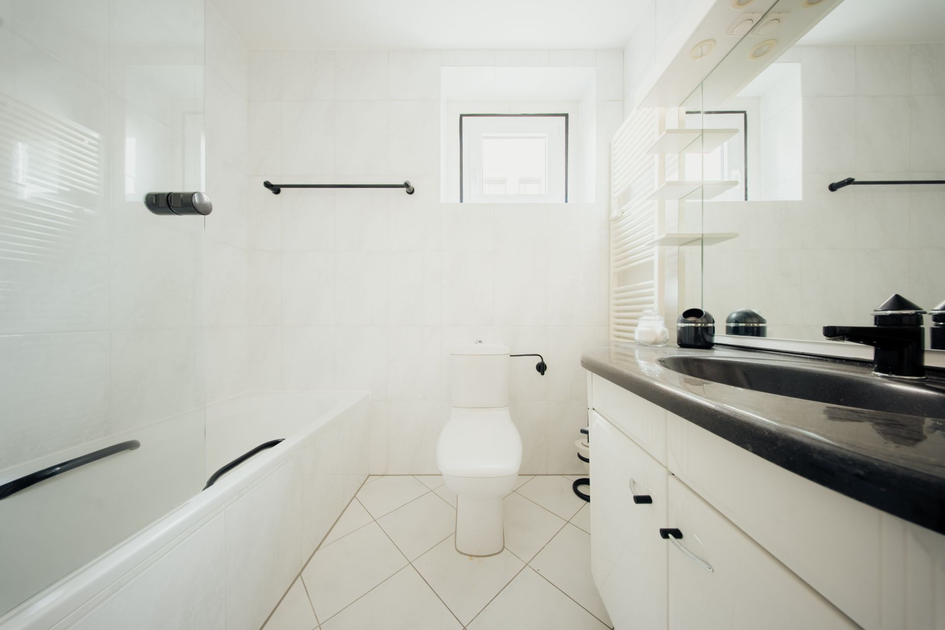 Helles Badezimmer mit Badewanne, Toilette, Waschbecken und Spiegel, zwei Fenster an der Wand.