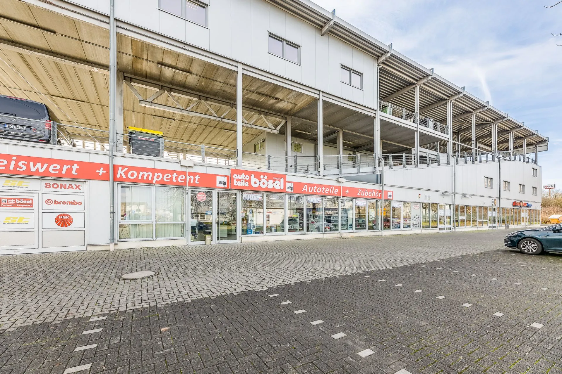 Modernes, zweistöckiges Gebäude mit großen Fenstern und Parkplätzen davor.