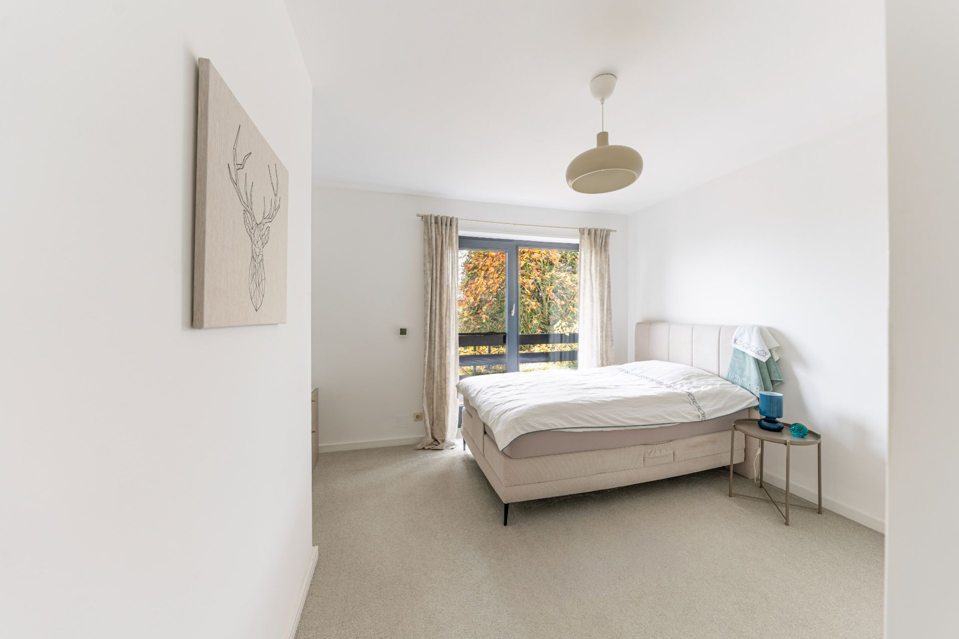 Helles Schlafzimmer mit Doppelbett, Nachttisch und großem Fenster mit Blick nach draußen.
