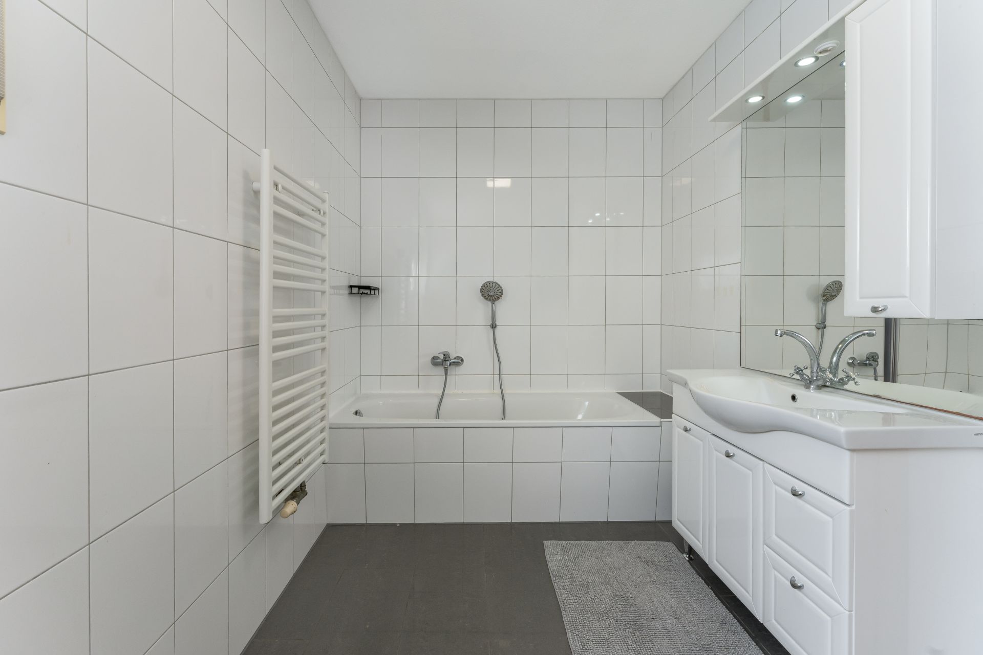 Modernes Badezimmer mit Badewanne, Waschbecken, Spiegelschrank und Handtuchheizkörper.