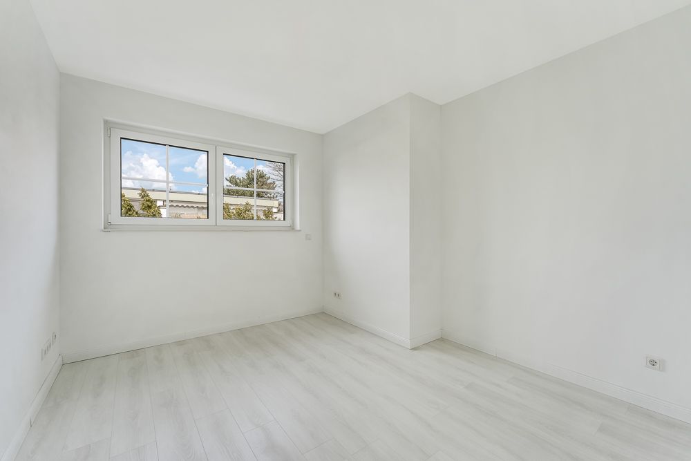 Heller, leerer Raum mit weißem Boden und zwei Fenstern an der Wand.