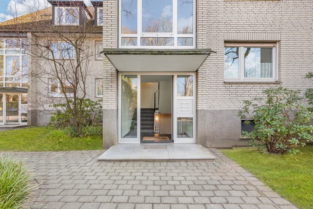Eingang eines Wohnhauses mit Glastür, Treppenhaus und umgebendem Garten.