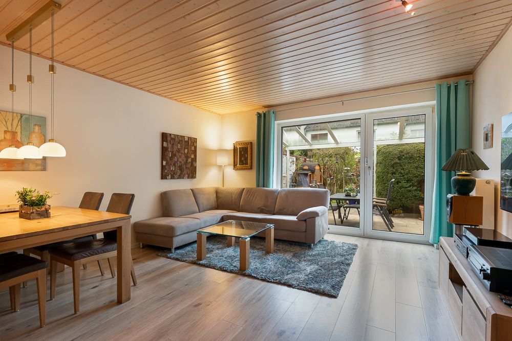 Modernes Wohnzimmer mit Ecksofa, Esstisch, Glastisch und Zugang zur Terrasse.