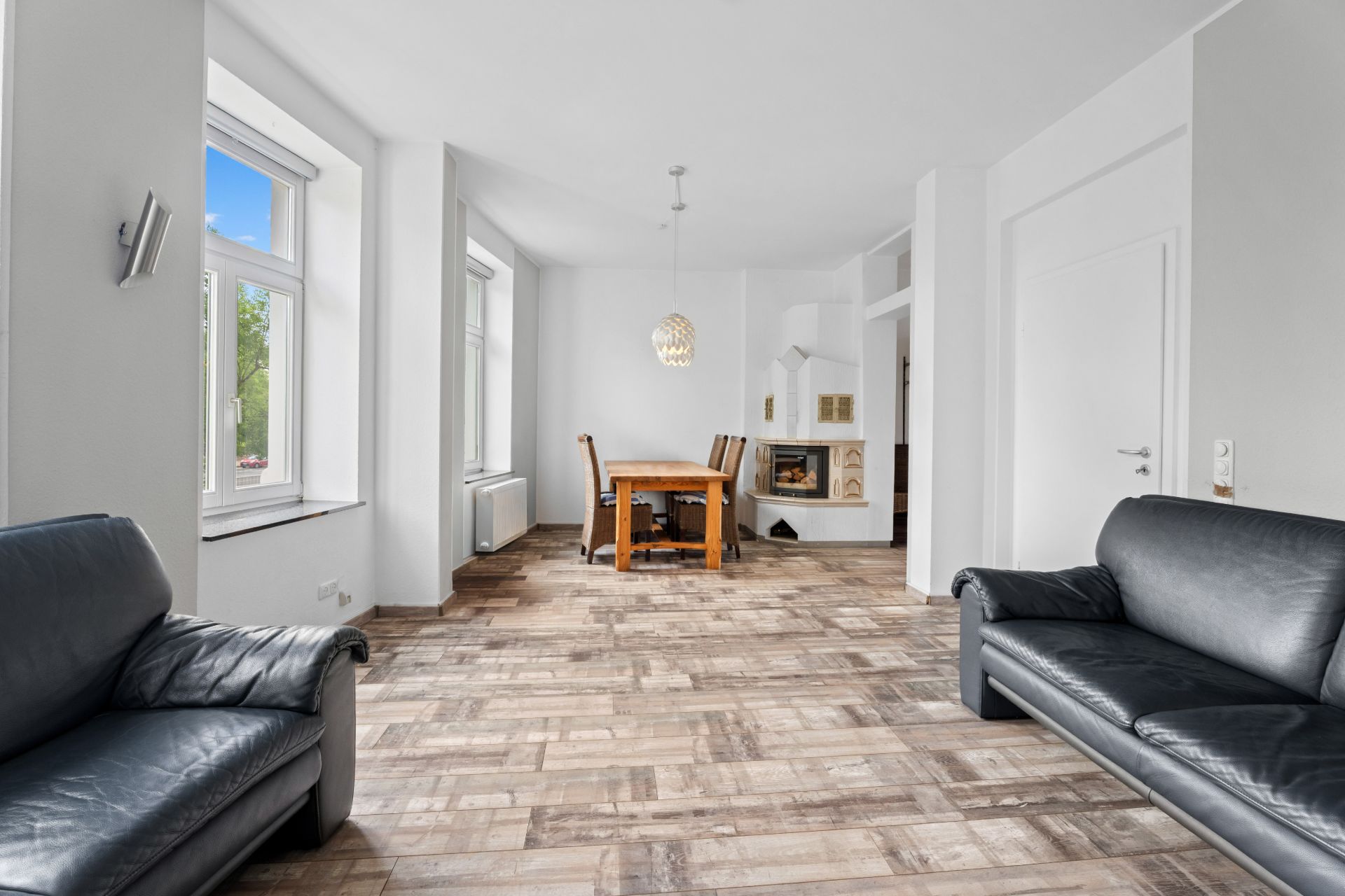 Heller Wohnraum mit zwei schwarzen Sofas, Holztisch mit Stühlen und großen Fenstern.