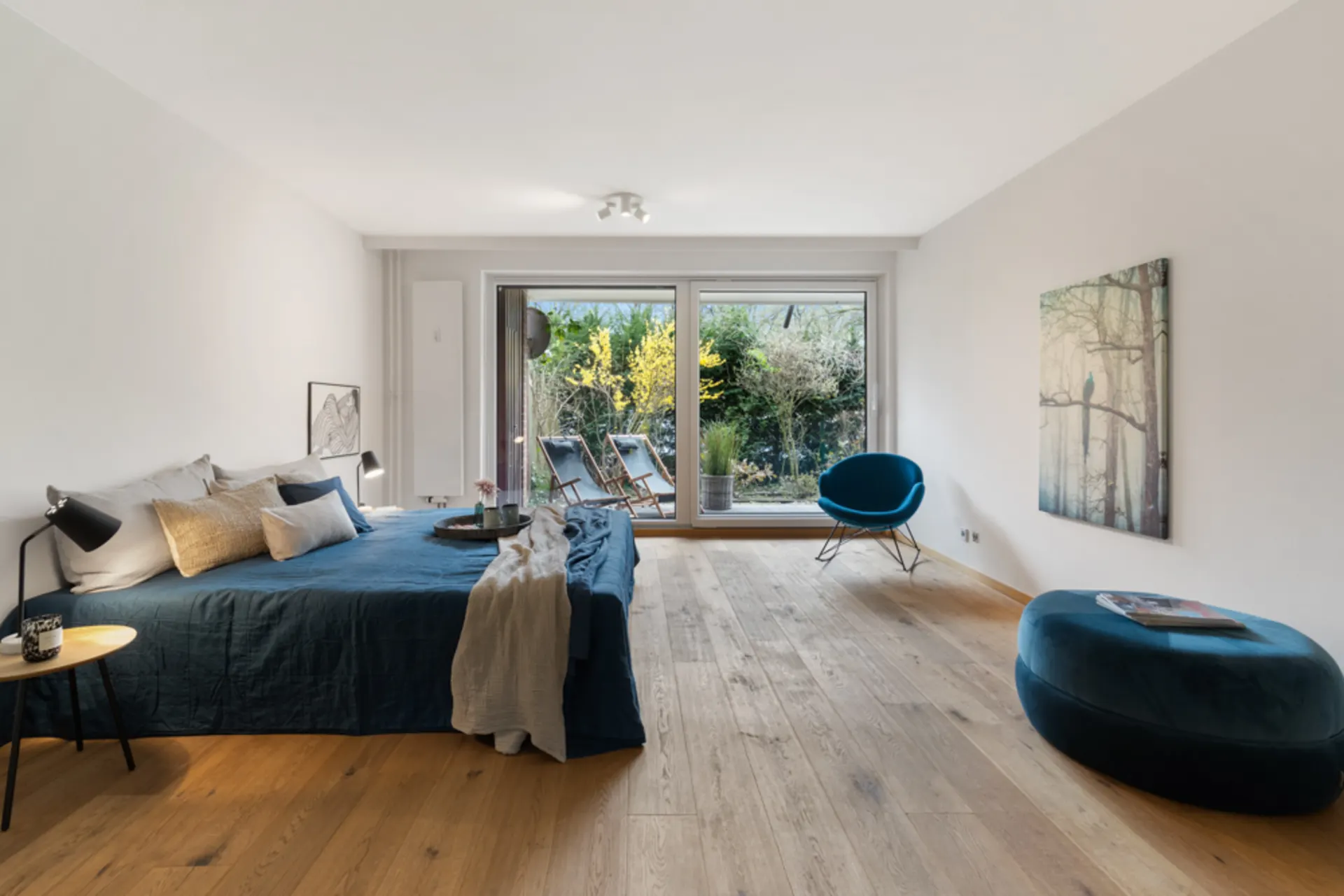 Helles Schlafzimmer mit großem Bett, Holzfußboden, Sessel und Zugang zum Garten durch Glasschiebetüren.