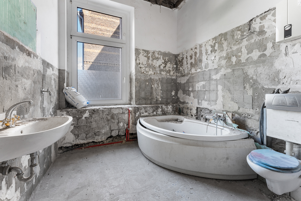 Badezimmer im Rohbau mit Badewanne, Waschbecken, Toilette und unverputzten Wänden.