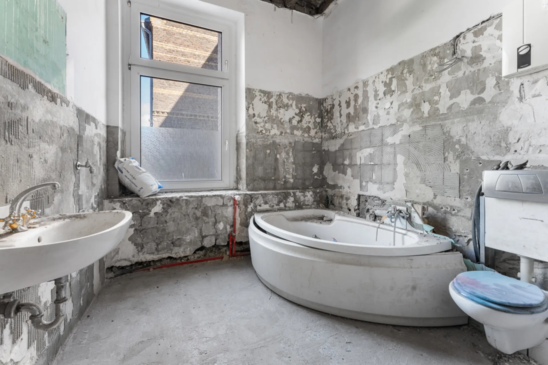 Badezimmer im Rohbau mit Badewanne, Waschbecken, Toilette und unverputzten Wänden.
