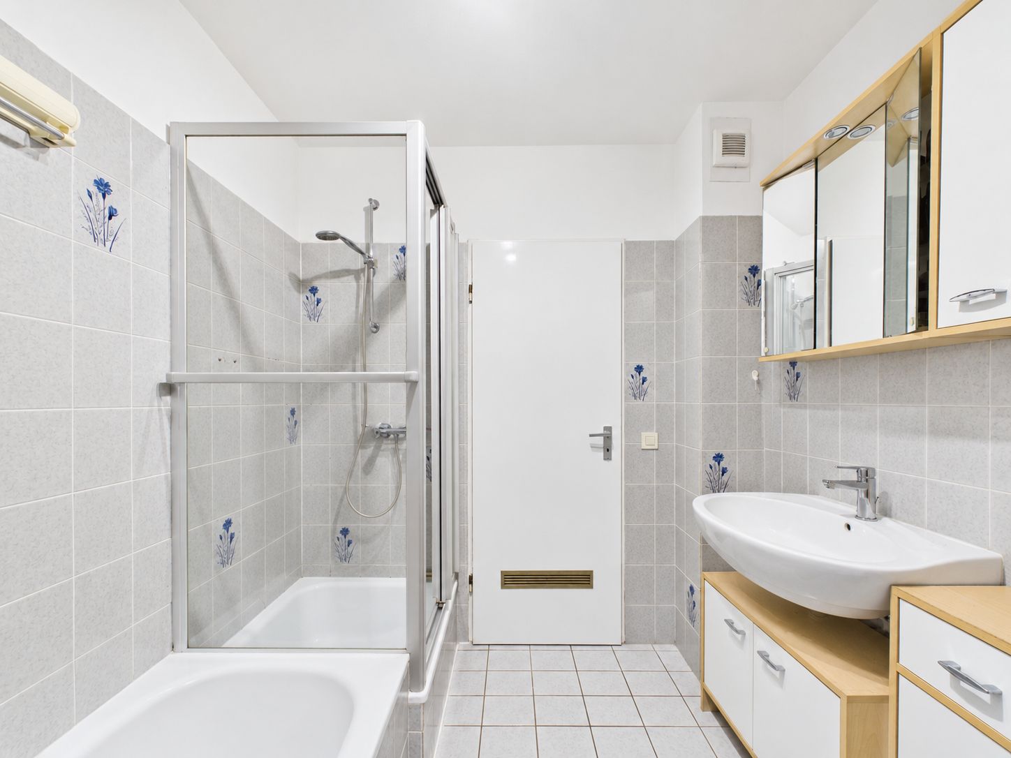 Modernes Badezimmer mit Badewanne, Dusche, Waschbecken und Spiegelschrank, graue Fliesen mit Blumenmuster.