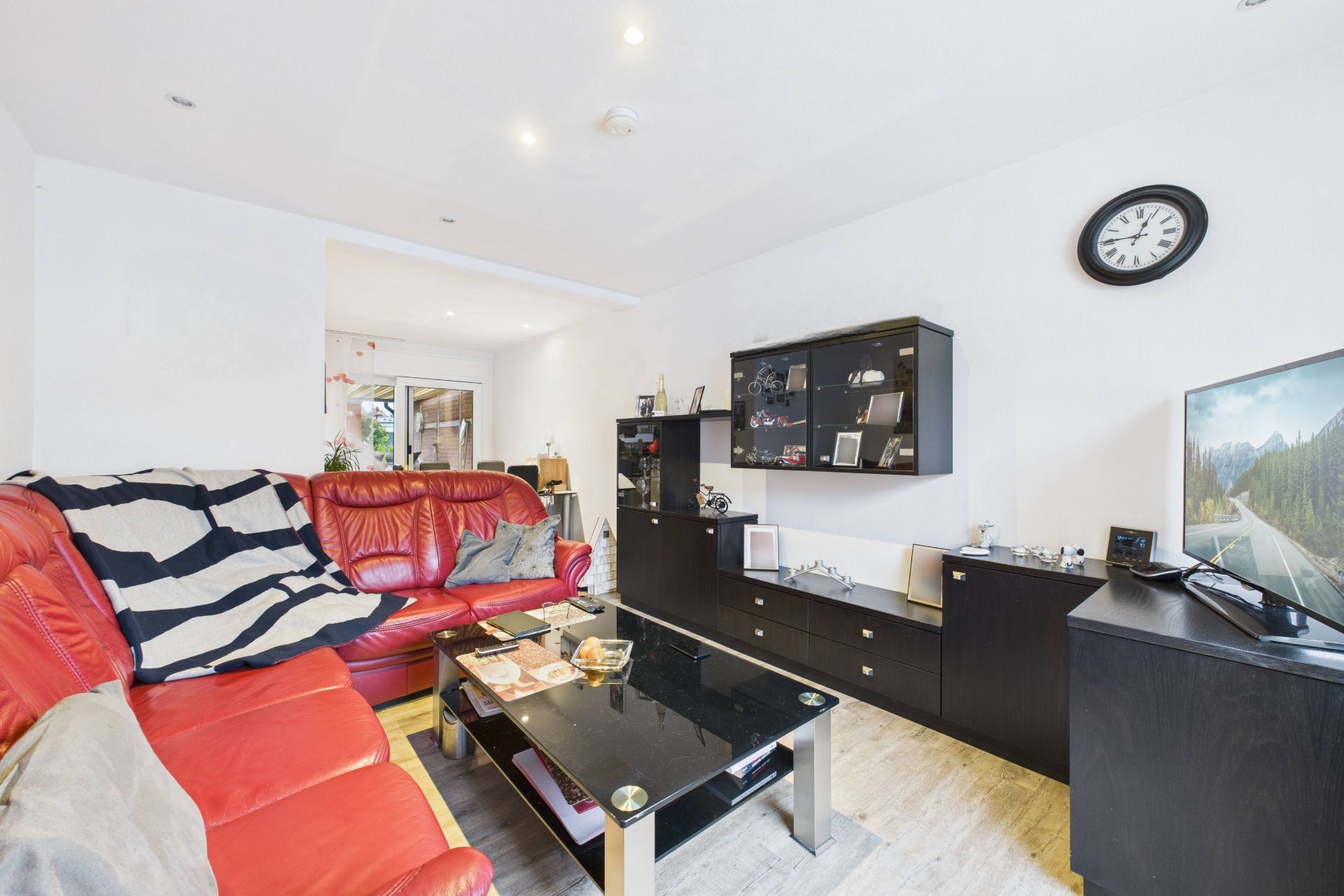 Wohnzimmer mit roten Ledersofas, schwarzem Couchtisch, Fernsehschrank und Wanduhr.