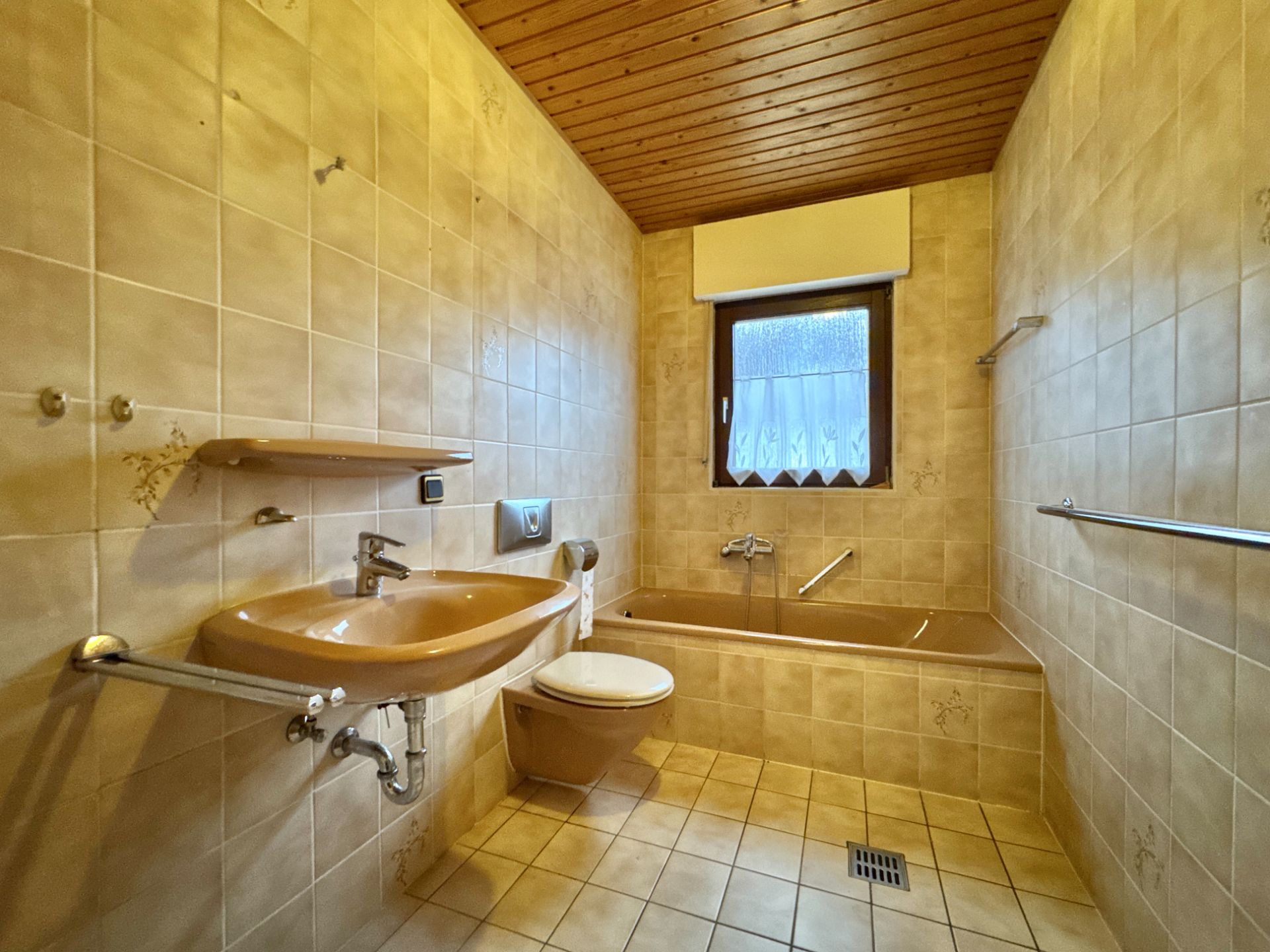 Badezimmer mit brauner Badewanne, Waschbecken, WC und Fenster, beige gefliest.