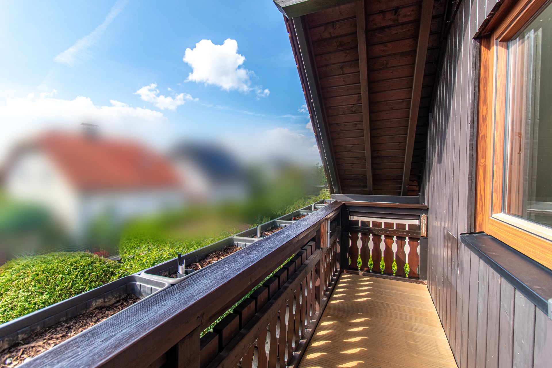 Balkon mit Holzgeländer und Dachschräge, Blick ins Grüne und auf Nachbarhäuser.