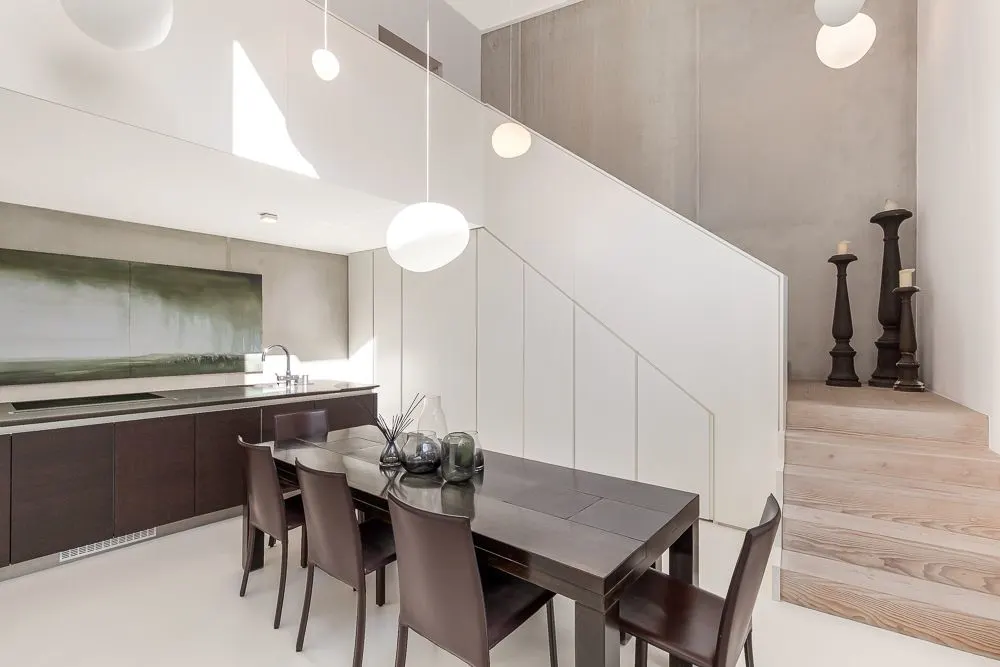 Modernes Esszimmer mit dunklem Tisch, sechs Stühlen und Treppe im Hintergrund.