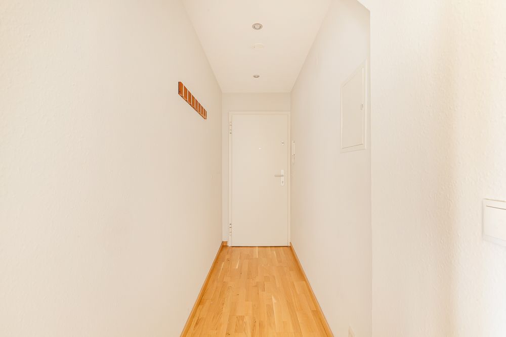 Heller Flur mit Holzboden, weißer Tür am Ende und Garderobenleiste an der Wand.
