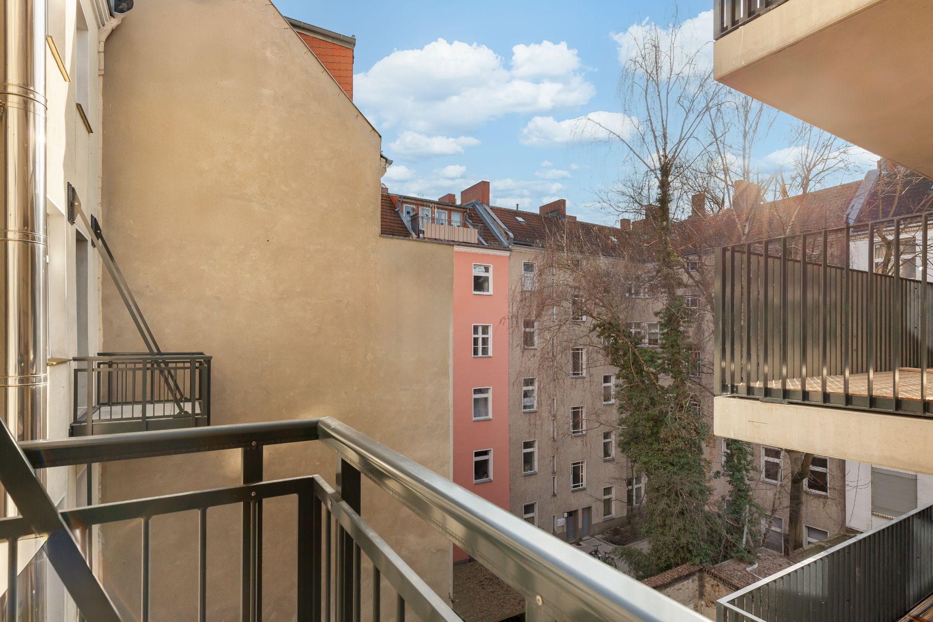 Blick von einem Balkon auf einen Innenhof mit mehreren Wohngebäuden und Bäumen.