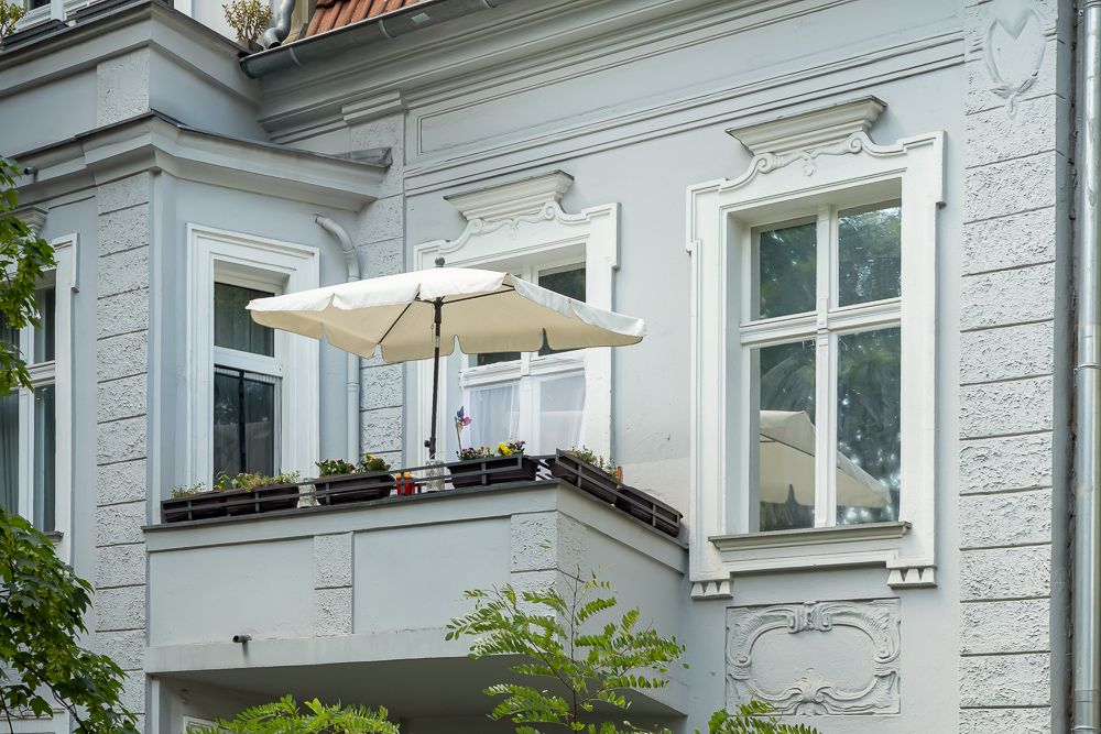Balkon mit Sonnenschirm, Blumenkästen und weißen Fenstern an einem Wohnhaus.