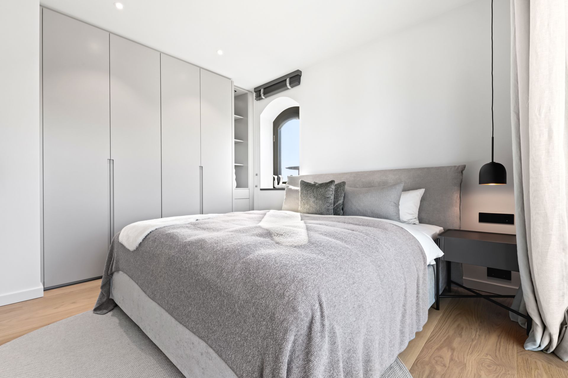 Modernes Schlafzimmer mit grauem Bett, Einbauschrank und Nachttisch mit Lampe.