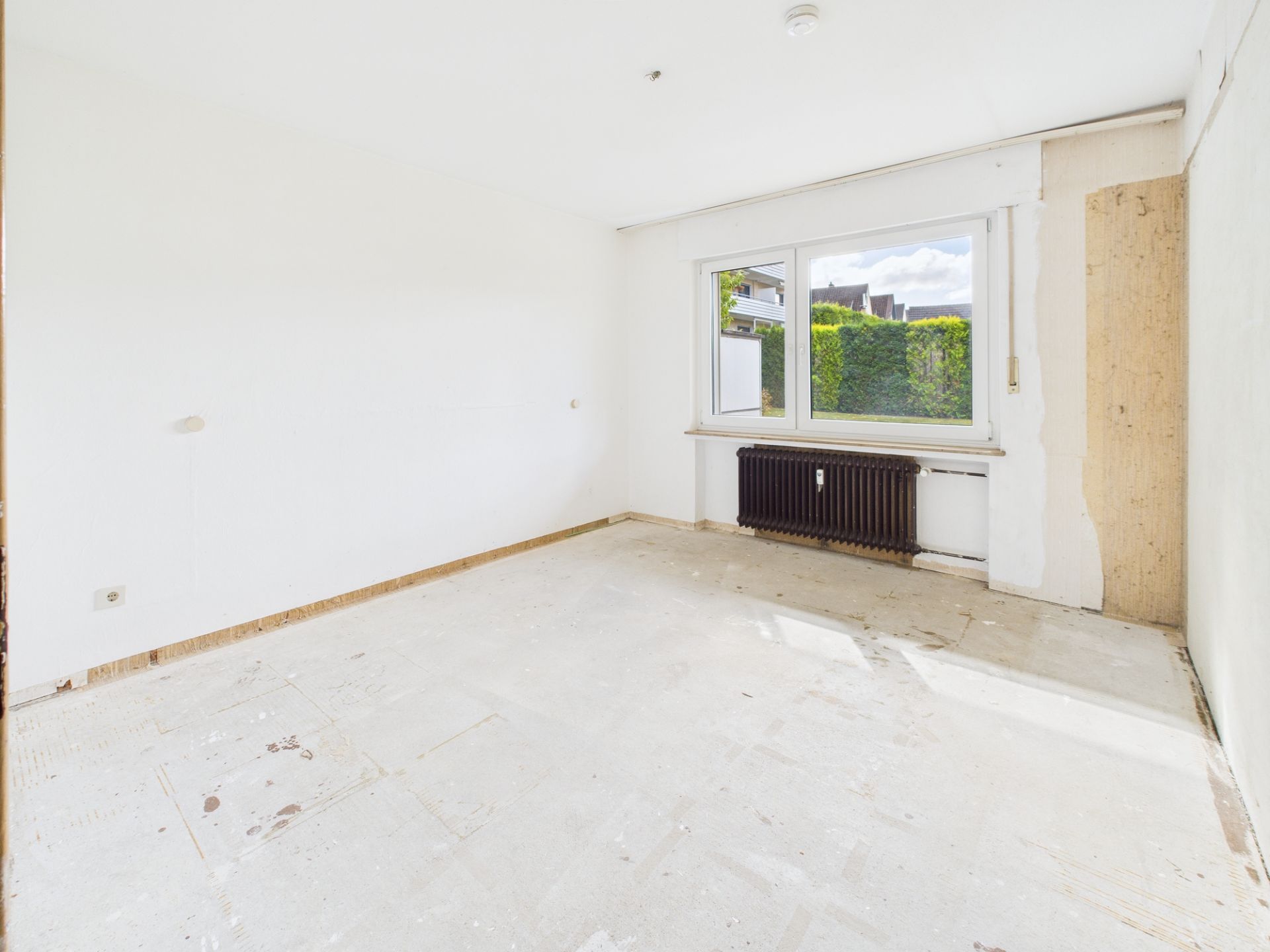 Leerer, heller Raum mit großem Fenster und sichtbarem Heizkörper unter dem Fenster.