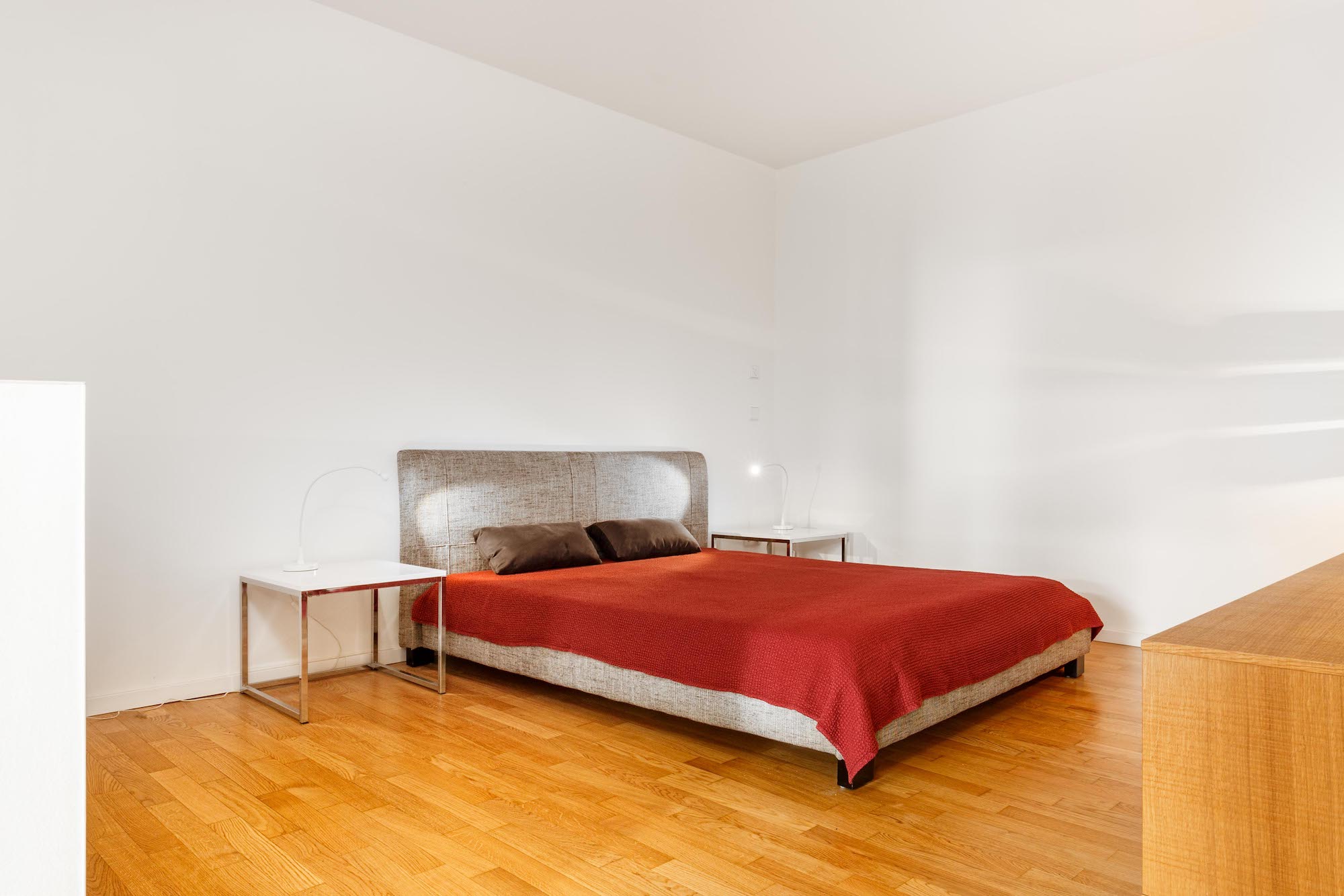 Schlafzimmer mit Doppelbett, roter Decke, zwei Nachttischen und Holzboden.