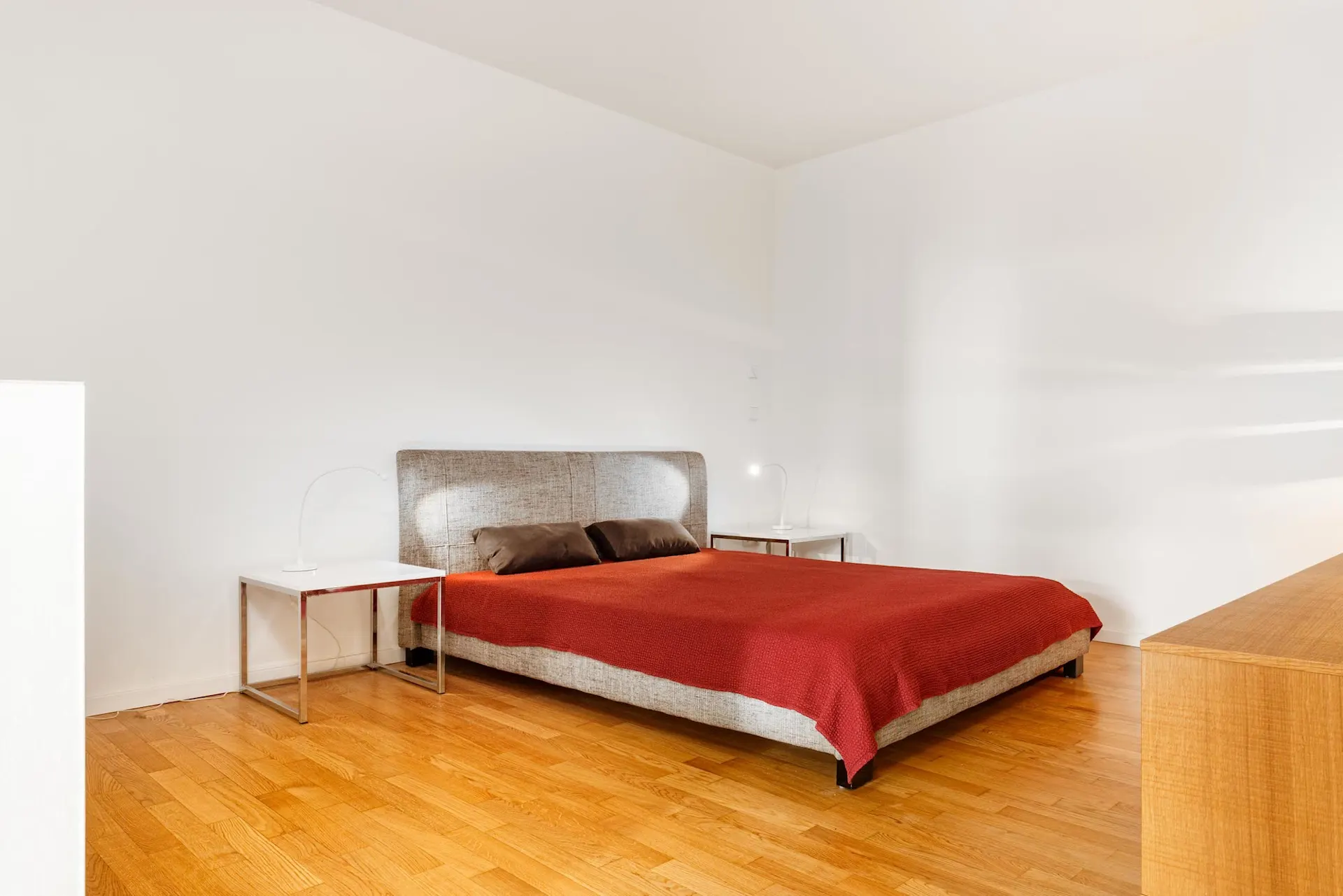 Schlafzimmer mit Doppelbett, roter Decke, zwei Nachttischen und Holzboden.