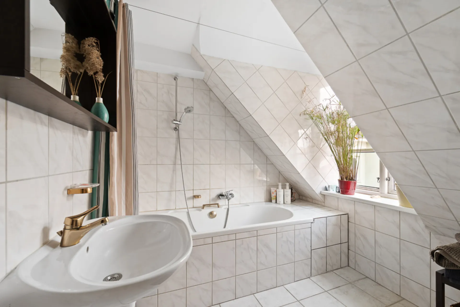 Helles Badezimmer mit Badewanne unter Dachschräge, Waschbecken und Pflanzen am Fenster.