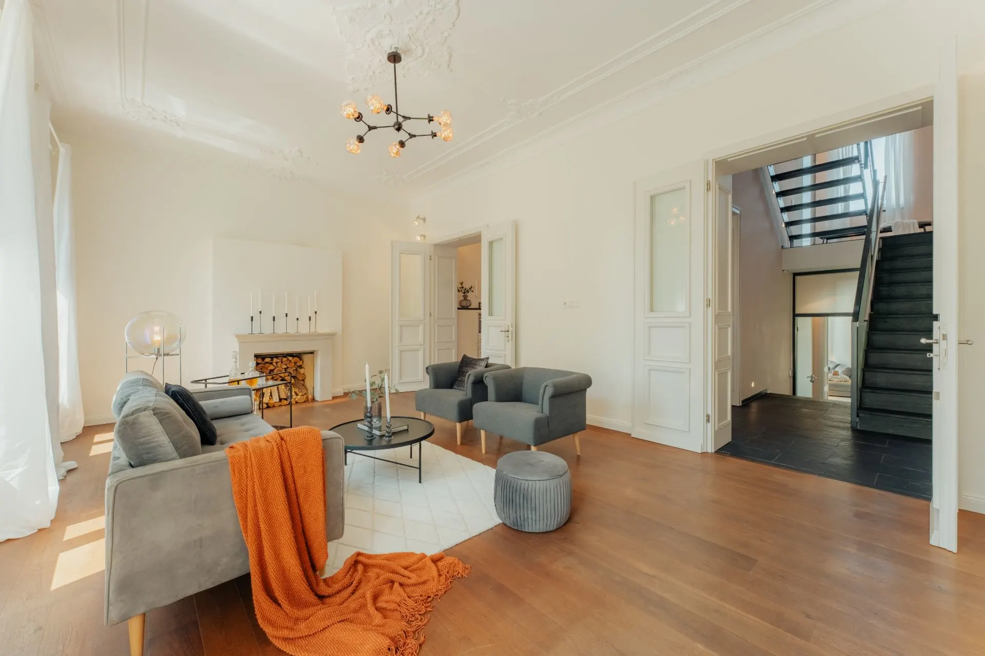 Helles Wohnzimmer mit grauem Sofa, Sessel, Couchtisch und Kamin auf Holzfußboden.