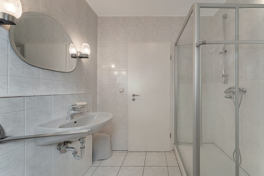 Modernes Badezimmer mit Dusche, Waschbecken, großem Spiegel und weißen Fliesen.