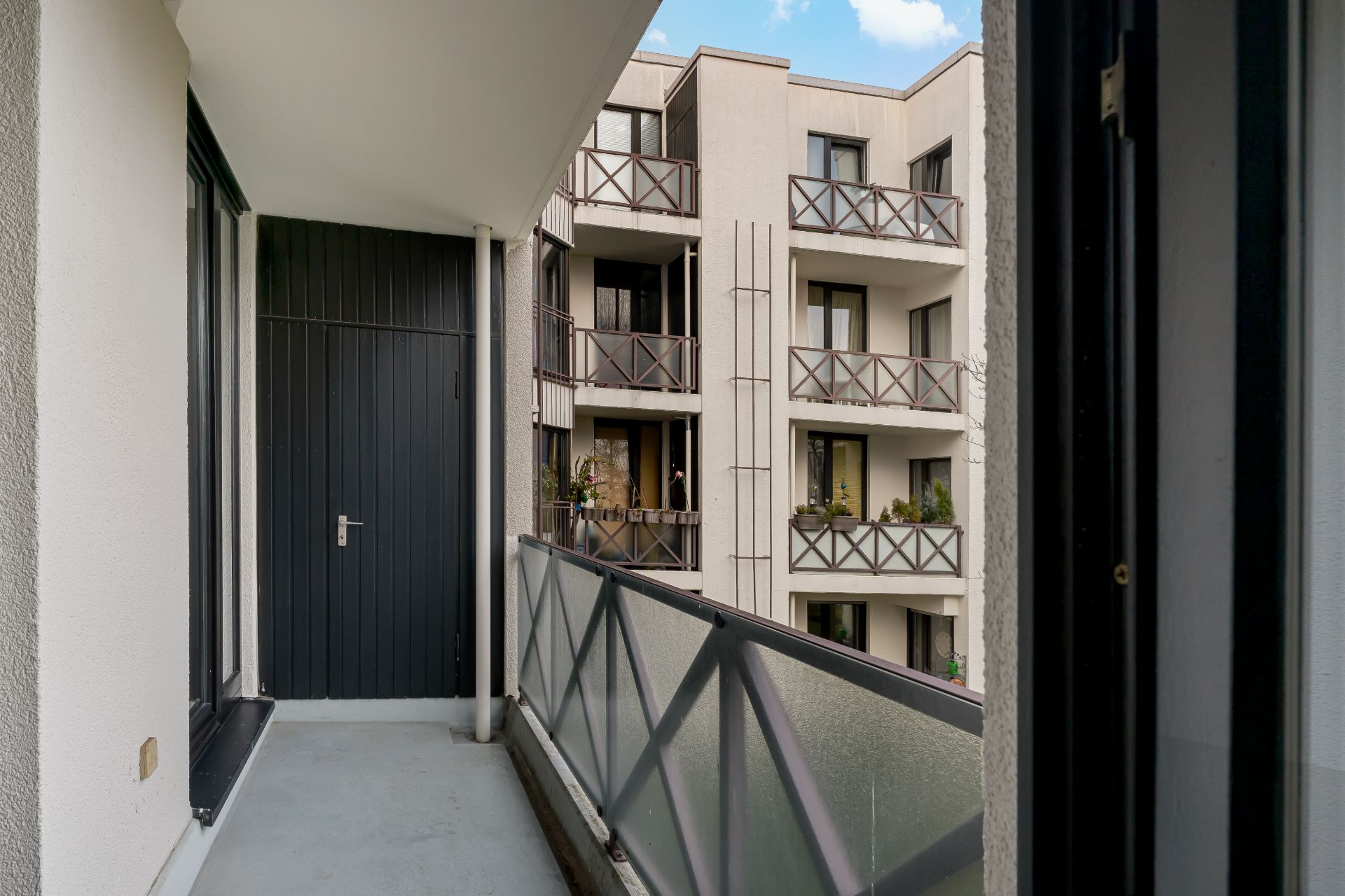 Balkon mit Glasgeländer und Blick auf Nachbarbalkone eines Wohnhauses.