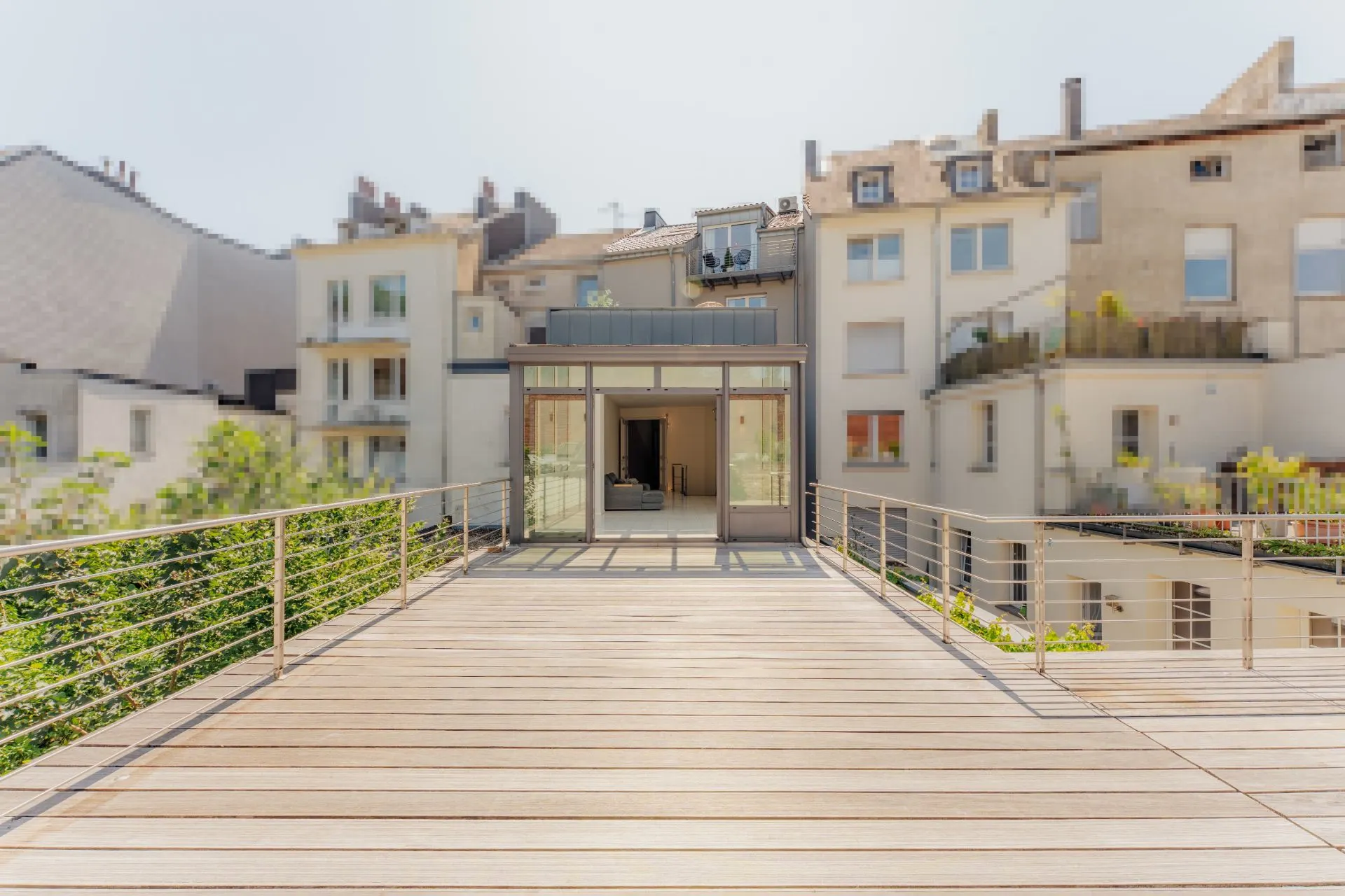Große Holzterrasse mit Metallgeländer und Blick auf urbane Wohnhäuser im Hintergrund.