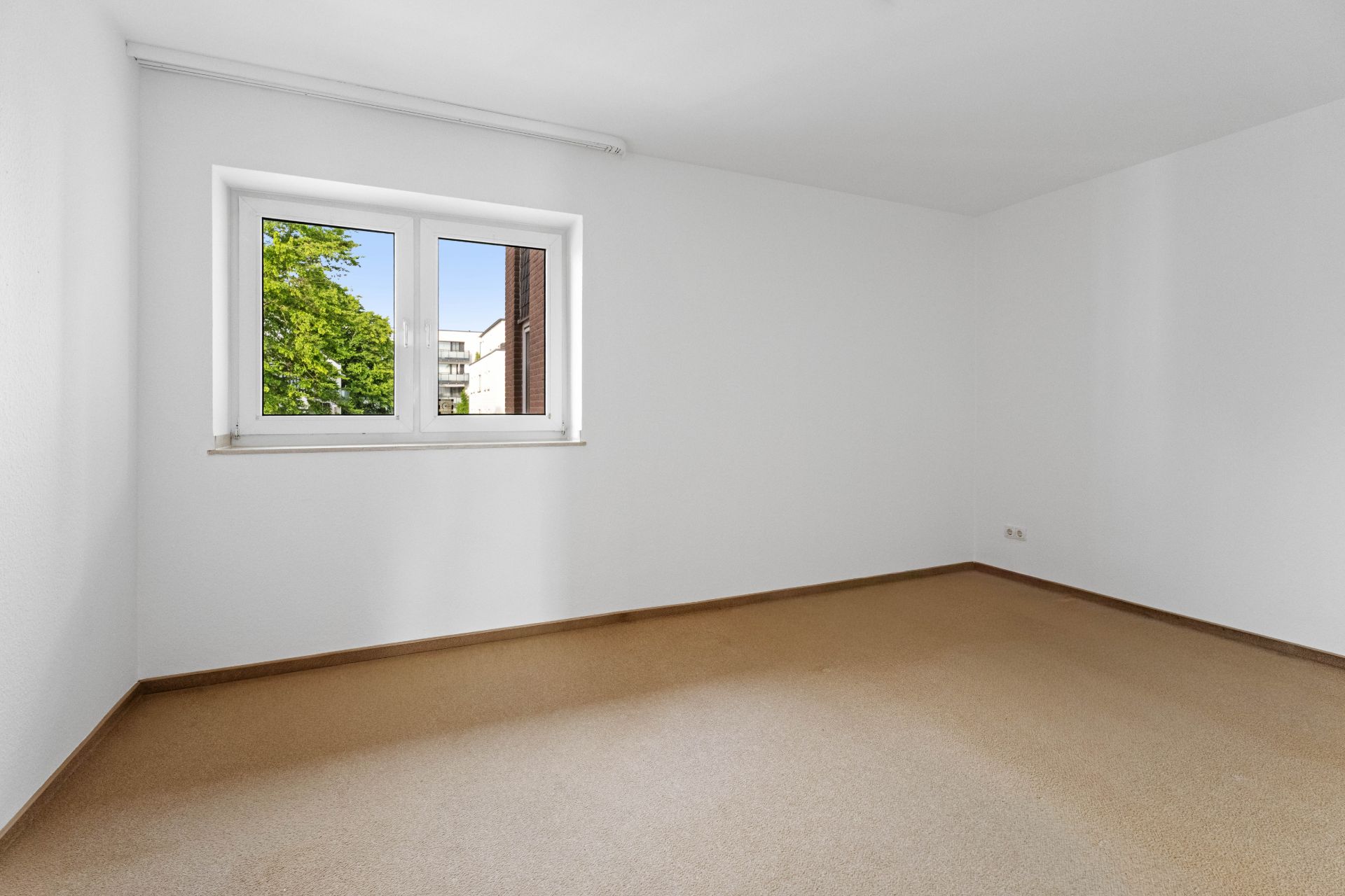 Leerer Raum mit beigem Teppichboden, weißem Fenster und weißen Wänden.