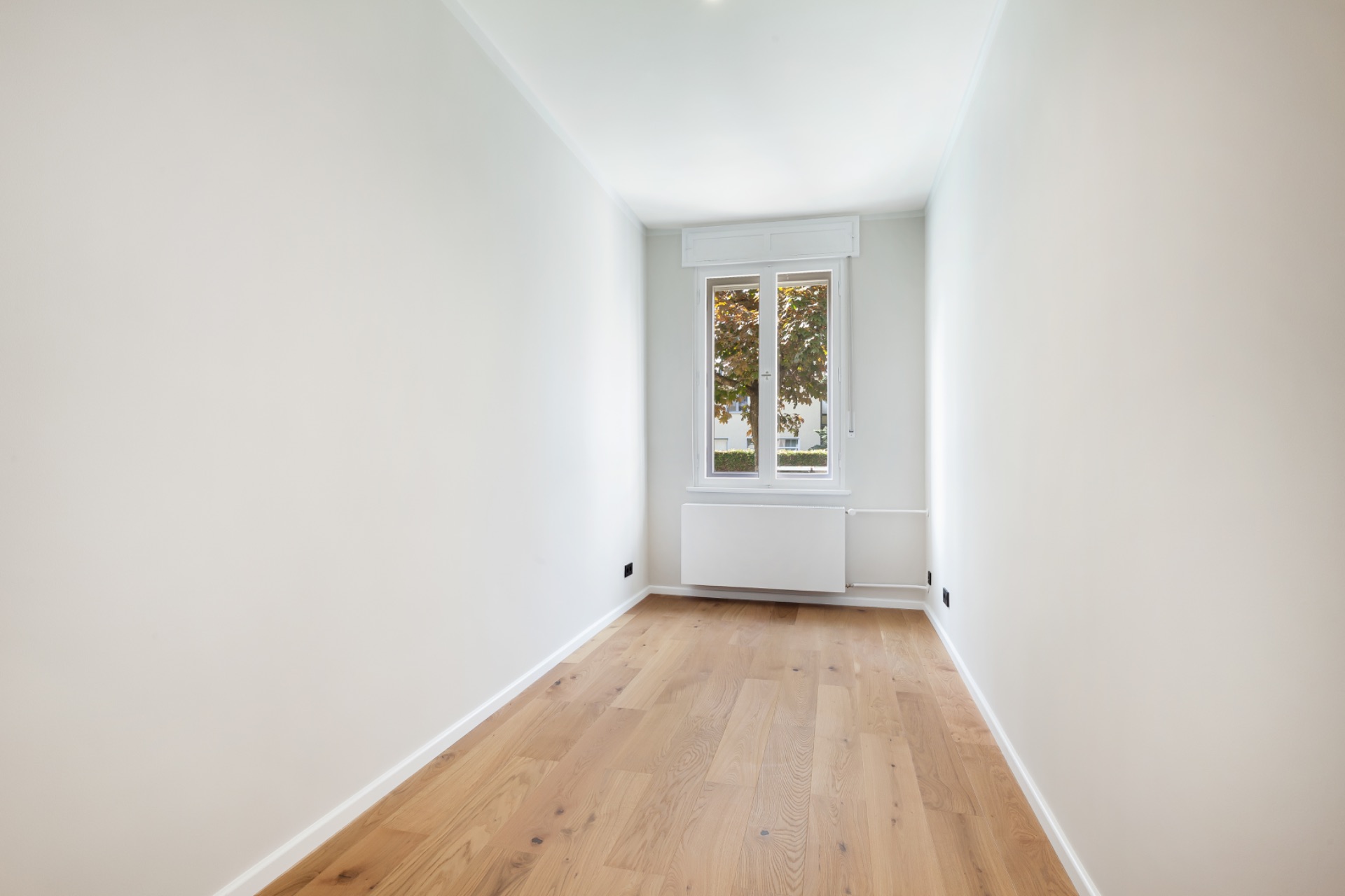 Heller, schmaler Raum mit Holzboden und Fenster am Ende.