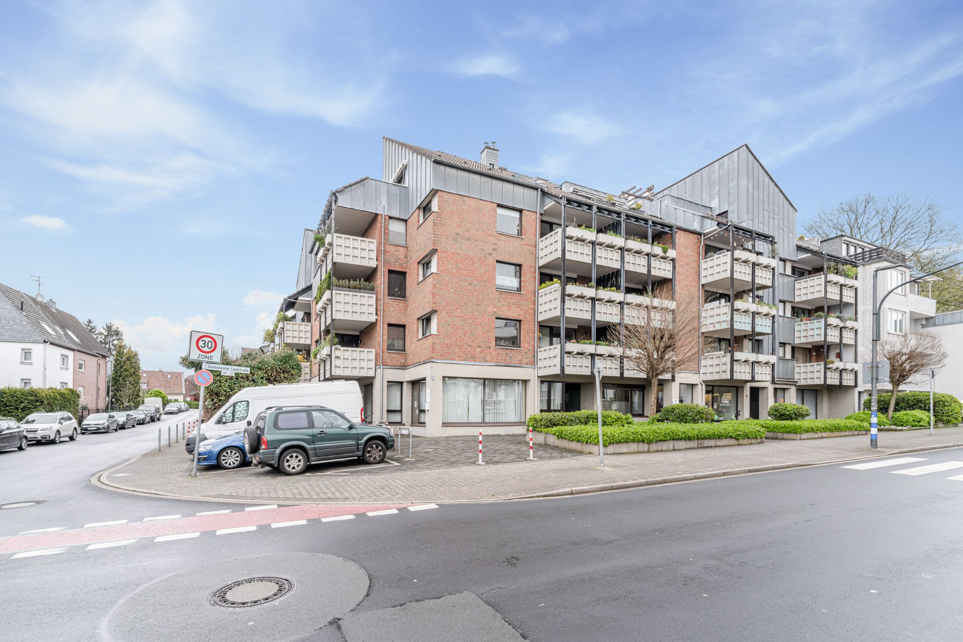Mehrstöckiges Wohnhaus mit Balkonen und geparkten Autos an einer Straßenecke.