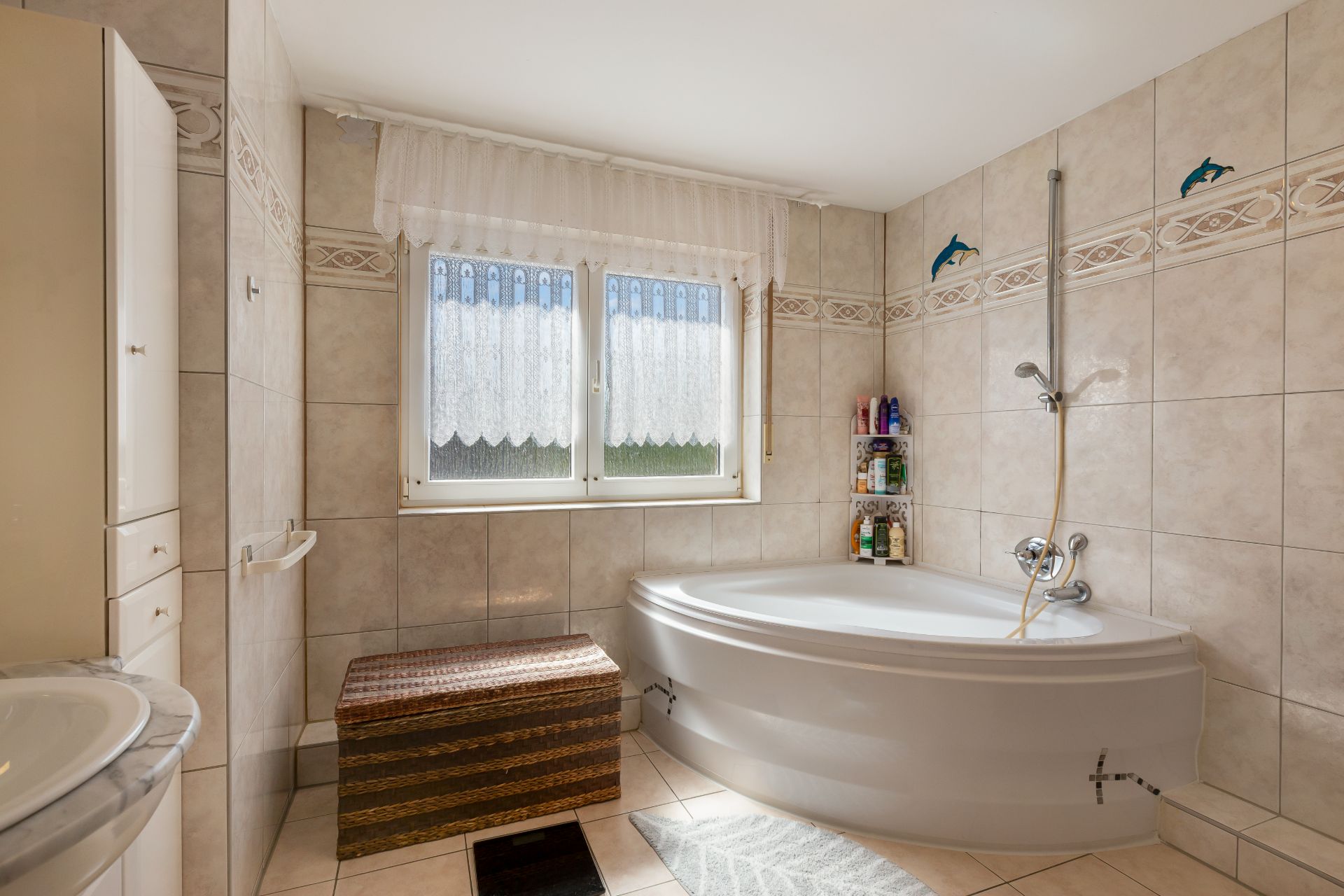 Helles Badezimmer mit Eckbadewanne, Fenster, gefliestem Boden und gefliesten Wänden.