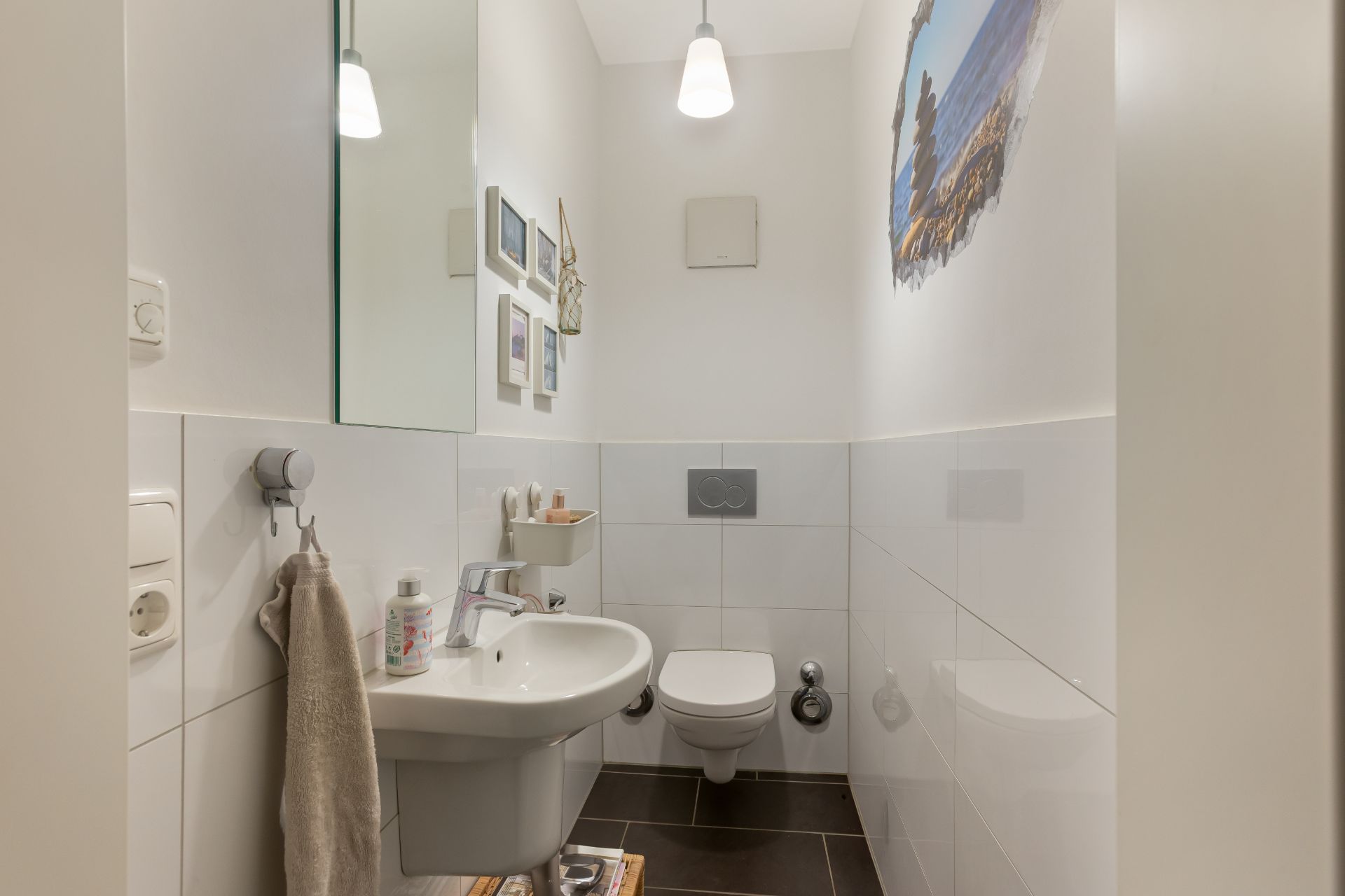 Kleines Badezimmer mit Hänge-WC, Waschbecken, Spiegel und Wandbildern.