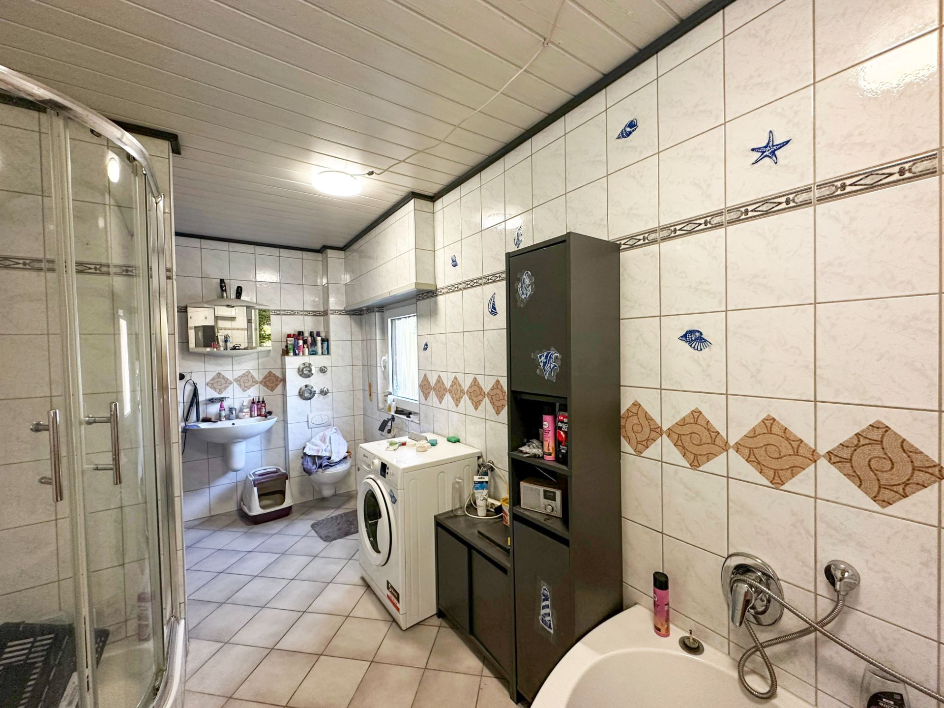 Modernes Badezimmer mit Dusche, Badewanne, Waschmaschine und Regal vor gefliester Wand.